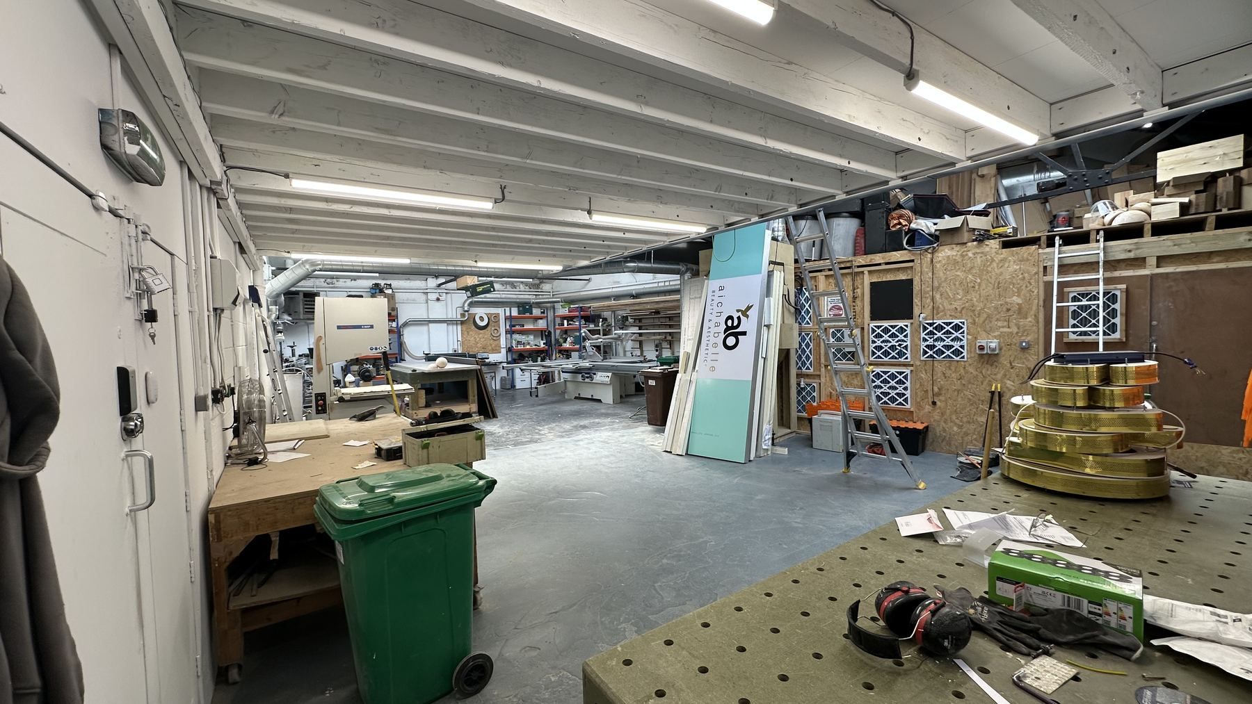 The machine shop at Milk Street: benches, bandsaw, panel saw and racking under strip lights