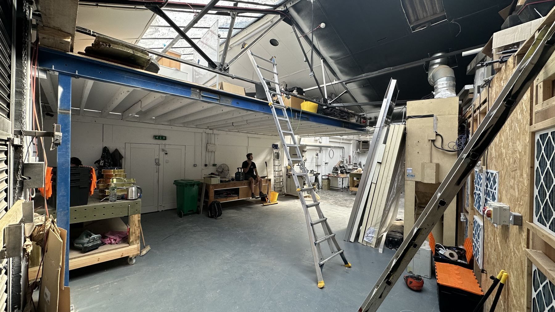 A maker at work under the mezzanine, with racking, ladders and tall panels