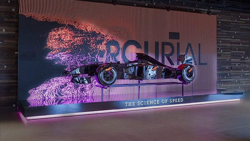 A race car on a lit display stand in front of a glowing particle backdrop