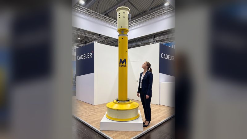A woman in a navy suit looking up at a tall yellow scale model of an offshore hammer on its plinth at an exhibition stand