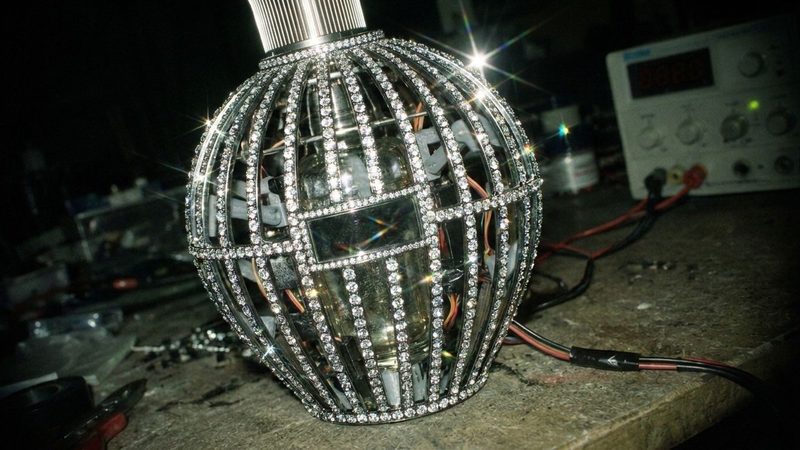 A crystal-studded flacon frame wired up on a workbench with a test meter beside it