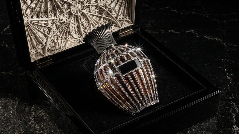 A black lacquered gift box opened to show a diamond-set perfume bottle on black velvet, with carved lace-like stonework inside the lid