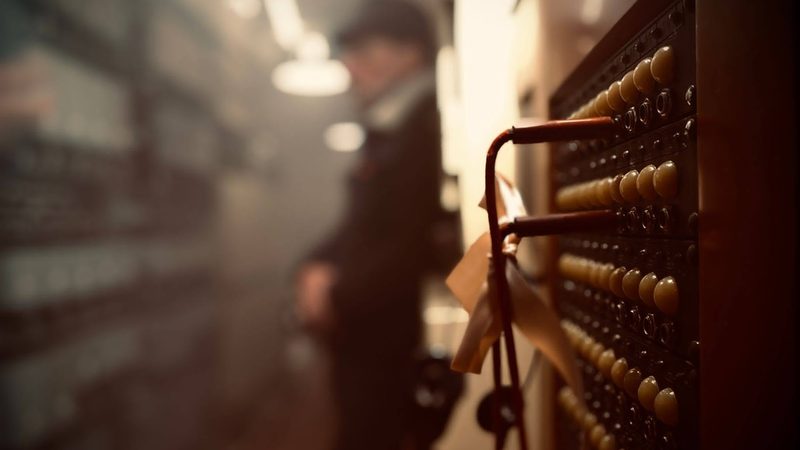 A 1950s telephone switchboard set with cream plug buttons and red cords, and a figure in a period coat behind it